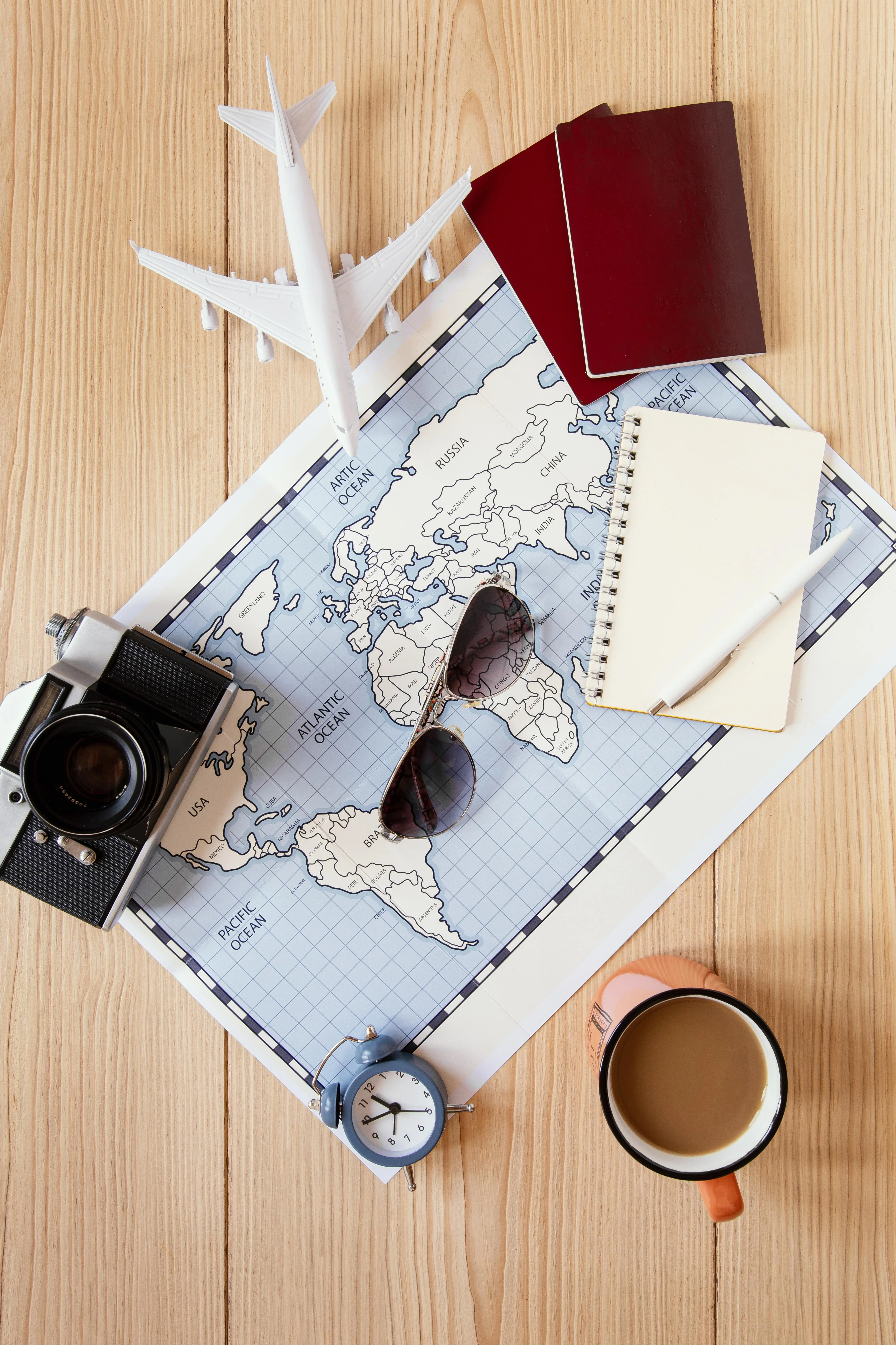 Elementos de un viaje apoyados sobre una mesa. Mapa, pasaporte, lentes de sol taza de café, reloj, camara de fotos, libreta con lapicera.